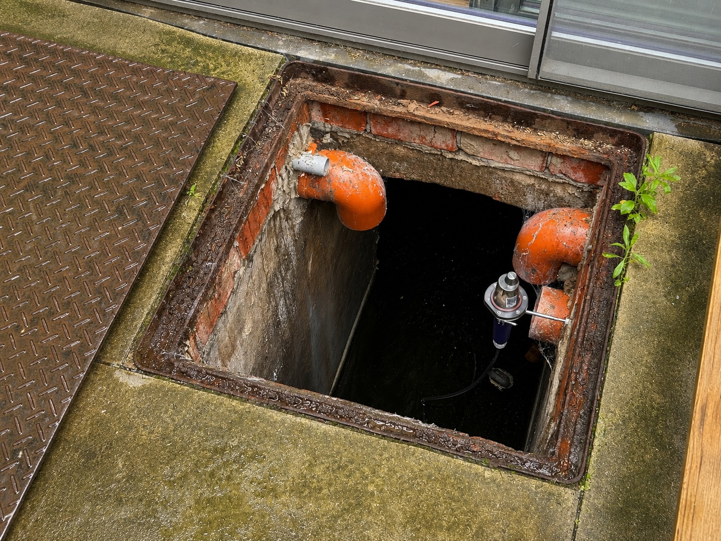 Open regenwaterput naast een woning, met een niveausensor aan een beugel boven het water